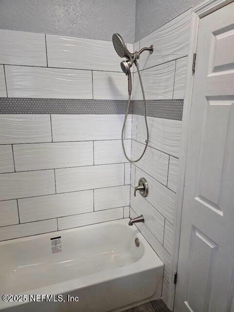 full bathroom featuring a textured wall and shower / bathtub combination