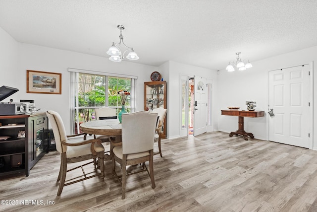 dining space with an inviting chandelier, baseboards, light wood finished floors, and a textured ceiling