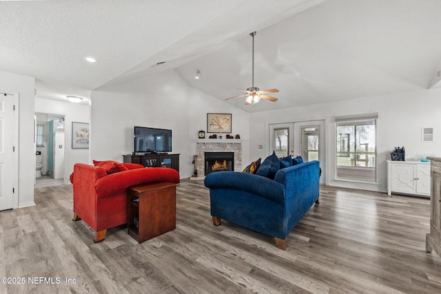 living area with a textured ceiling, high vaulted ceiling, a stone fireplace, wood finished floors, and visible vents