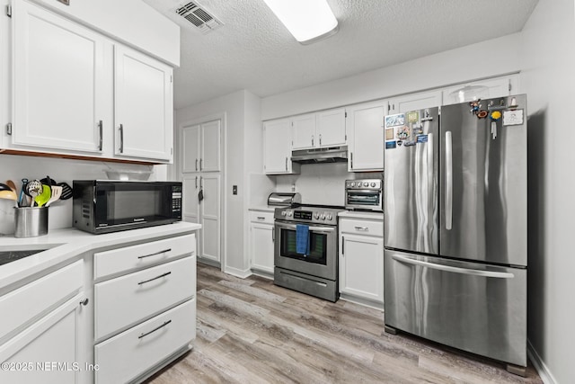 kitchen featuring stainless steel appliances, light countertops, light wood-type flooring, under cabinet range hood, and white cabinetry