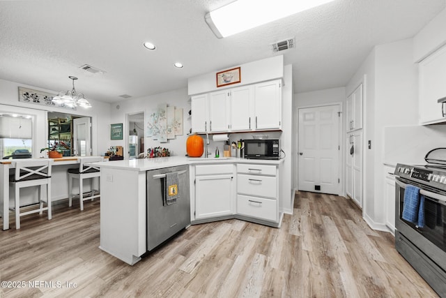 kitchen with visible vents, appliances with stainless steel finishes, light wood-style floors, white cabinetry, and a peninsula