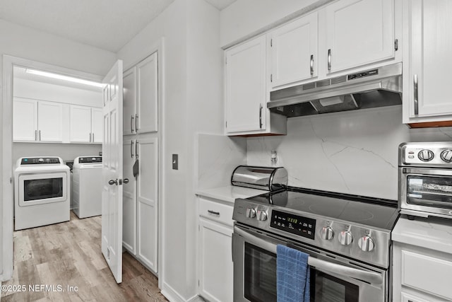 kitchen featuring washing machine and dryer, stainless steel range with electric cooktop, under cabinet range hood, and white cabinetry