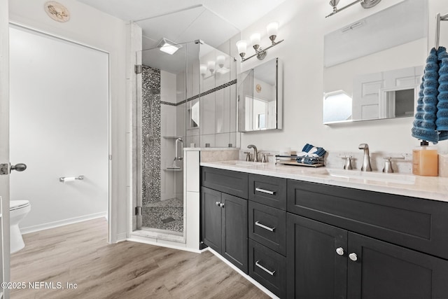 bathroom with double vanity, a stall shower, a sink, and wood finished floors