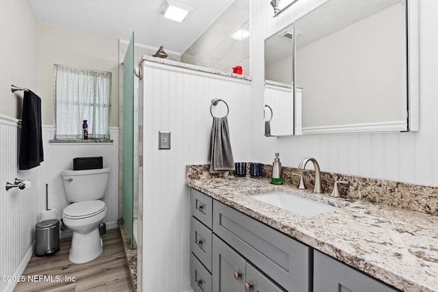 full bathroom featuring a wainscoted wall, wood finished floors, toilet, vanity, and a walk in shower