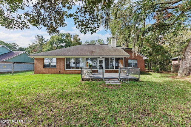 back of house featuring a sunroom, a chimney, a lawn, and brick siding