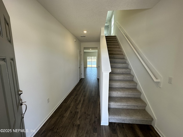 stairway with a textured ceiling, baseboards, and wood finished floors