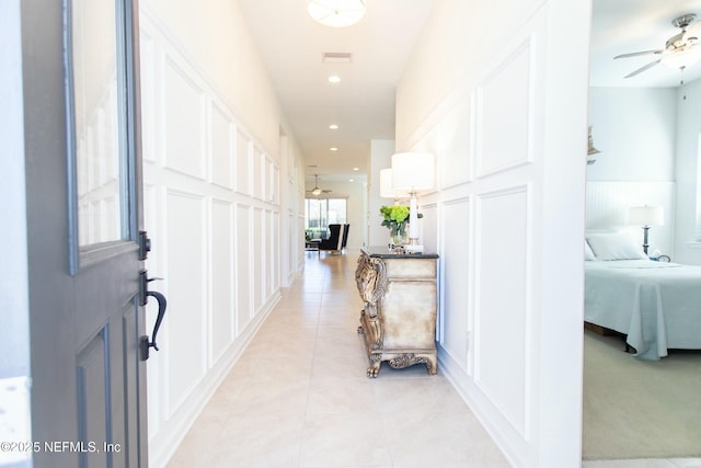 hall with light tile patterned floors, a decorative wall, recessed lighting, and visible vents