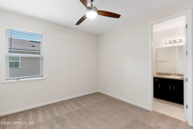 unfurnished bedroom featuring baseboards, ensuite bathroom, a sink, and light colored carpet