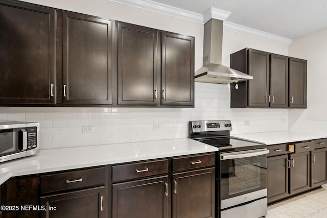 kitchen featuring light countertops, appliances with stainless steel finishes, ornamental molding, dark brown cabinetry, and wall chimney range hood