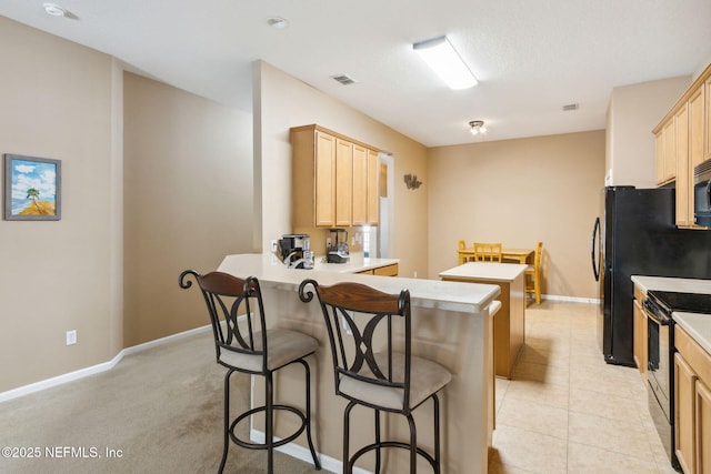 kitchen with visible vents, a breakfast bar, a peninsula, light brown cabinetry, and black electric range