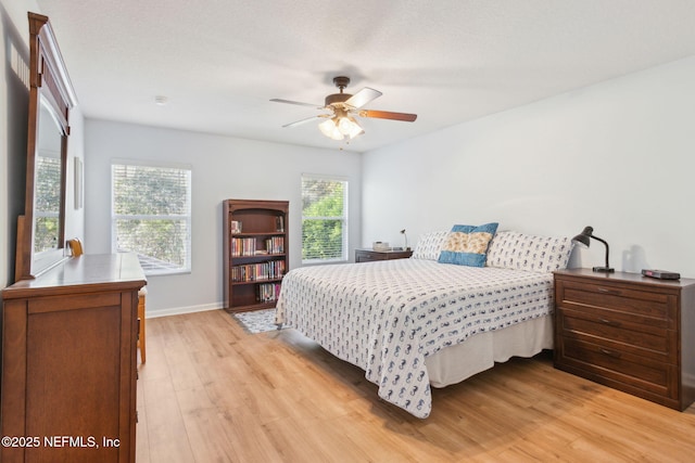 bedroom with light wood finished floors, a ceiling fan, and baseboards