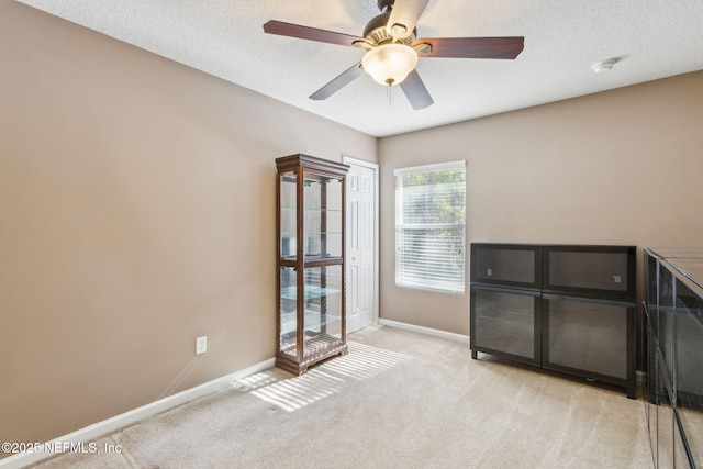 unfurnished room with ceiling fan, baseboards, a textured ceiling, and light colored carpet