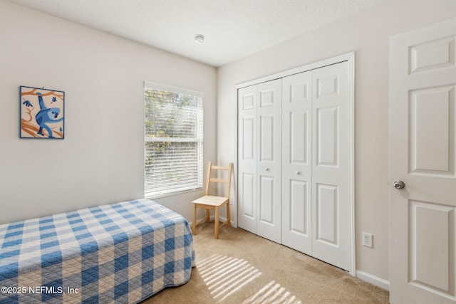 bedroom featuring baseboards, a closet, a textured ceiling, and light colored carpet