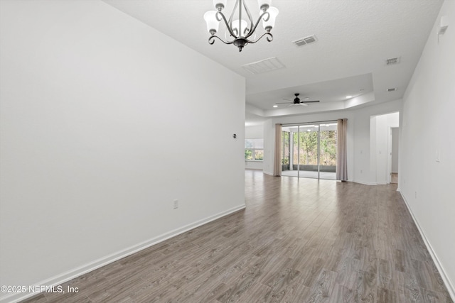 unfurnished room featuring light wood-style flooring, visible vents, a raised ceiling, and baseboards