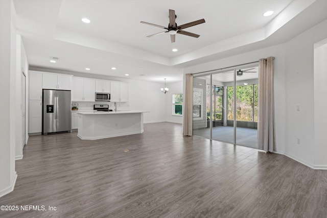 unfurnished living room featuring ceiling fan with notable chandelier, dark wood-style flooring, a raised ceiling, and baseboards