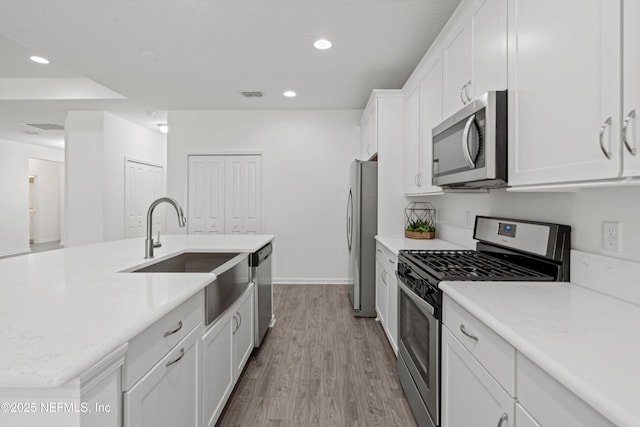 kitchen featuring recessed lighting, appliances with stainless steel finishes, white cabinetry, a sink, and wood finished floors