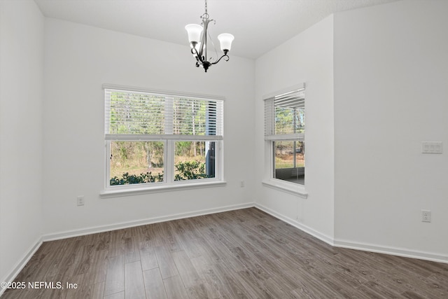 spare room featuring baseboards, a chandelier, and wood finished floors