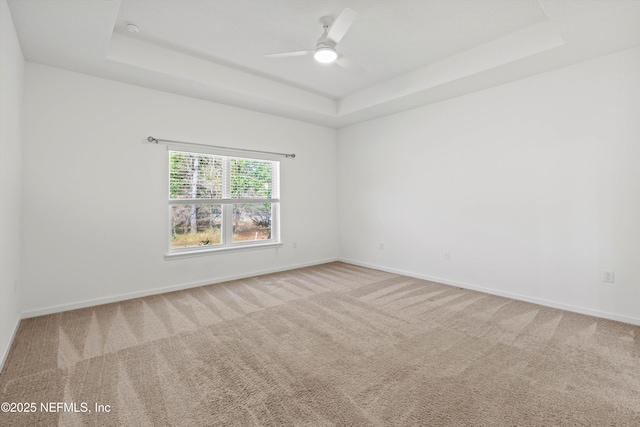 spare room featuring carpet floors, a tray ceiling, baseboards, and a ceiling fan