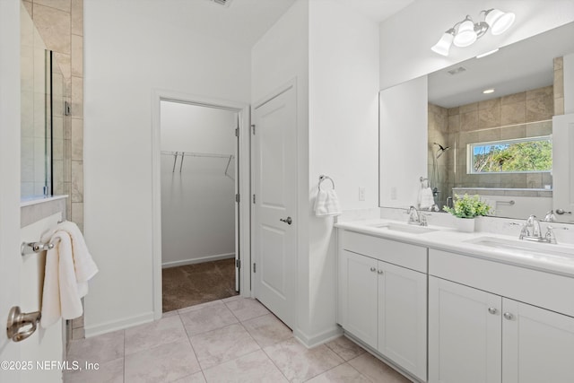 bathroom featuring a walk in closet, double vanity, a tile shower, and a sink