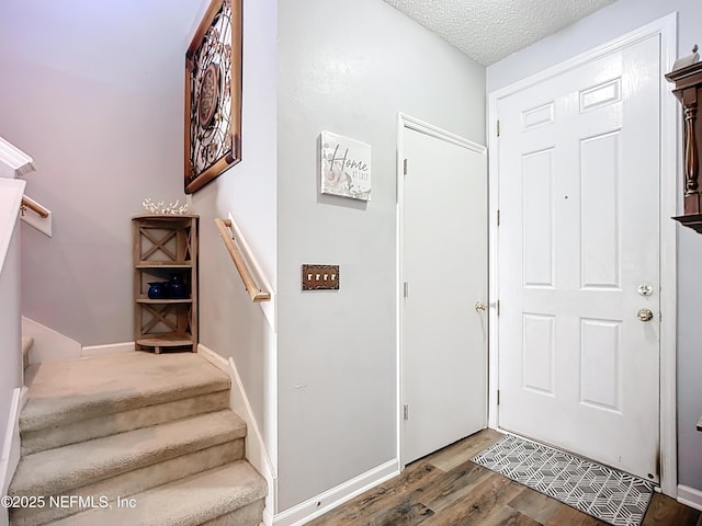 foyer with baseboards, a textured ceiling, wood finished floors, and stairs