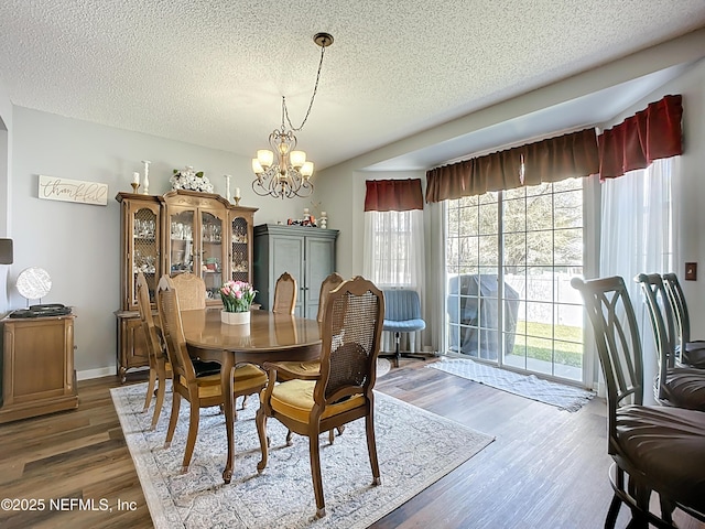 dining area with baseboards, wood finished floors, a textured ceiling, and a chandelier