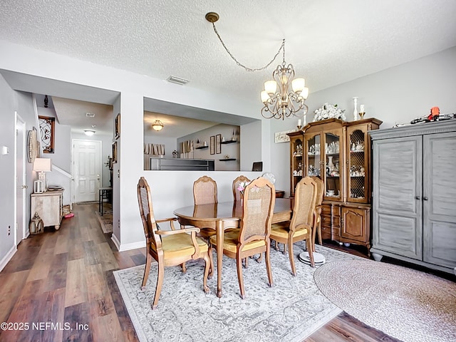 dining room with visible vents, baseboards, dark wood finished floors, an inviting chandelier, and a textured ceiling