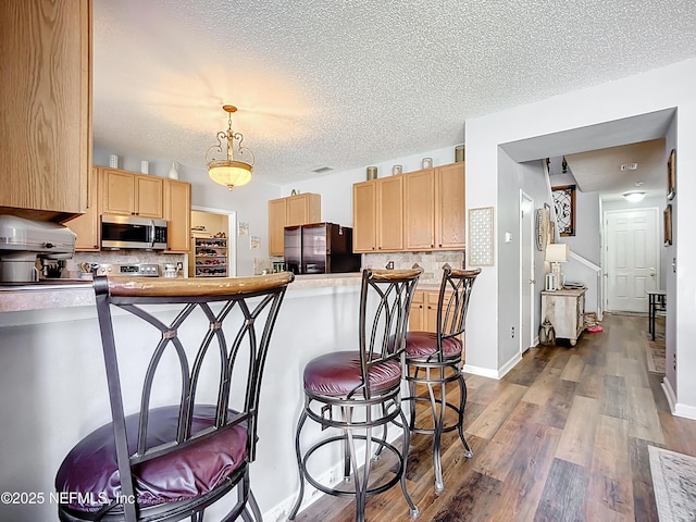 kitchen with dark wood-style floors, light brown cabinetry, stainless steel appliances, a kitchen bar, and tasteful backsplash