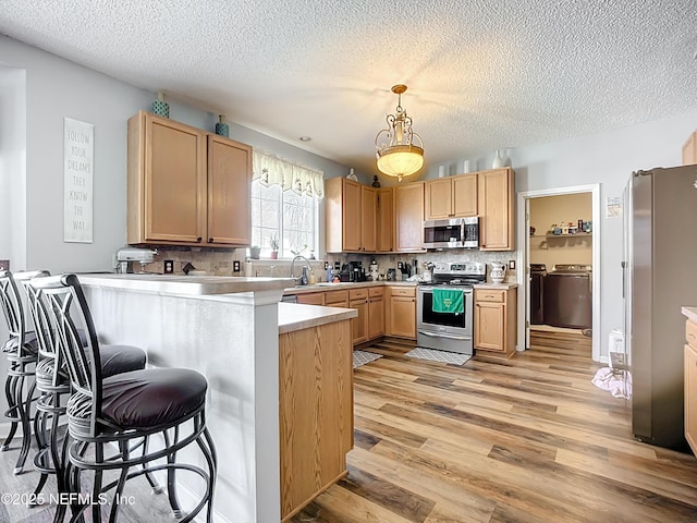 kitchen with a breakfast bar, appliances with stainless steel finishes, a peninsula, light wood-style floors, and separate washer and dryer