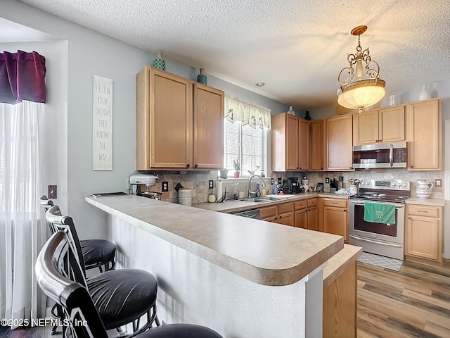 kitchen featuring a peninsula, a sink, light countertops, appliances with stainless steel finishes, and a kitchen breakfast bar