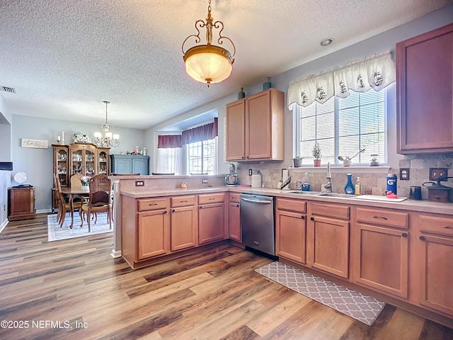 kitchen featuring a peninsula, light countertops, light wood-style floors, dishwasher, and a chandelier