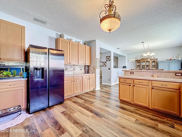 kitchen with visible vents, light wood-type flooring, an inviting chandelier, light countertops, and stainless steel fridge