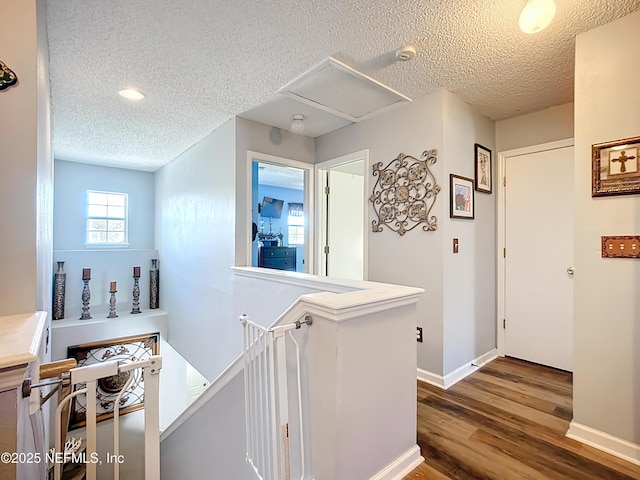 hall featuring baseboards, an upstairs landing, a textured ceiling, and wood finished floors