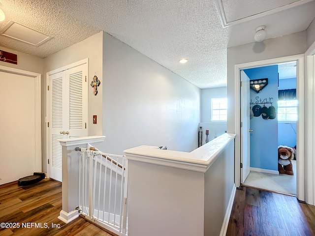 hall with an upstairs landing, a textured ceiling, and dark wood-style flooring