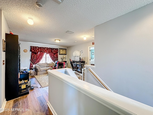 hall featuring an upstairs landing, visible vents, light wood-style flooring, and a textured ceiling