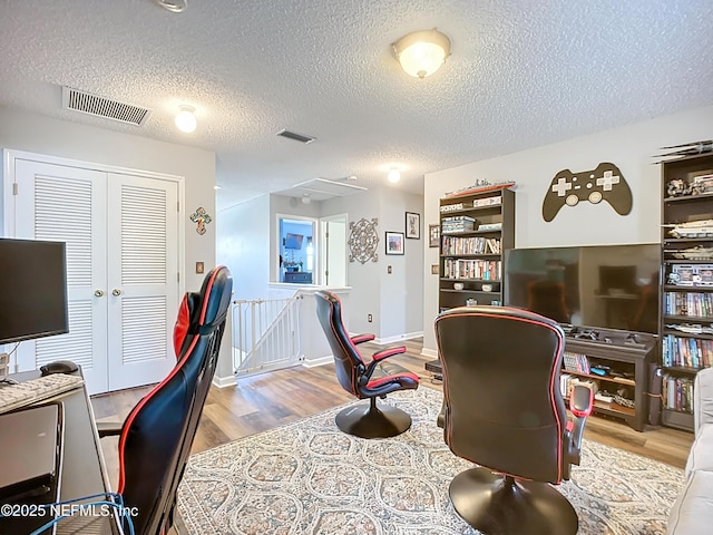 home office with visible vents, baseboards, a textured ceiling, and wood finished floors