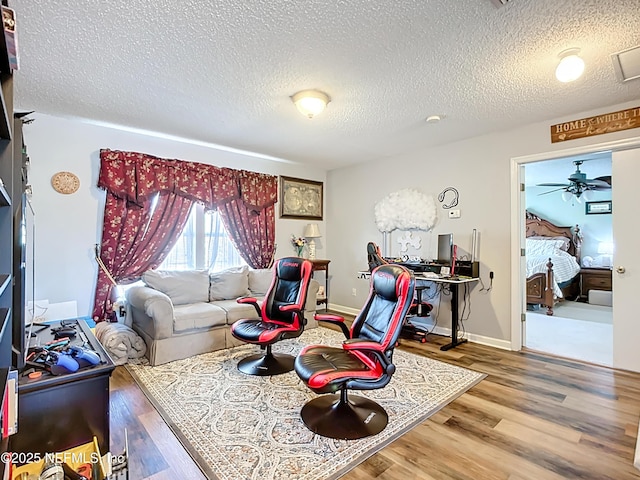 living area with baseboards, a textured ceiling, wood finished floors, and a ceiling fan