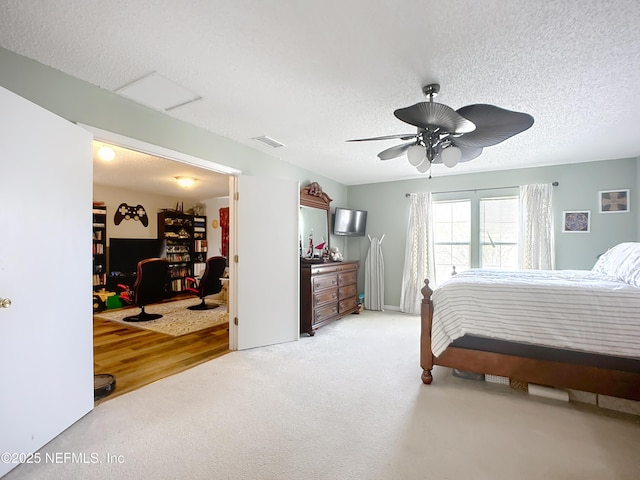 bedroom featuring a ceiling fan, light colored carpet, visible vents, and a textured ceiling