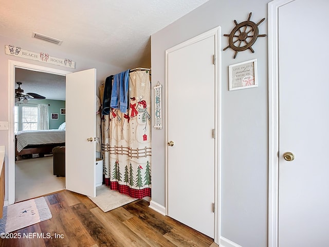 hallway featuring wood finished floors, visible vents, and a textured ceiling