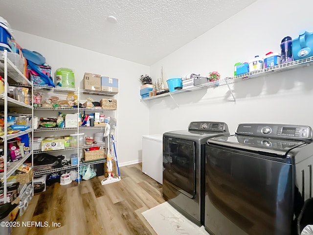 clothes washing area with laundry area, a textured ceiling, light wood-type flooring, and separate washer and dryer