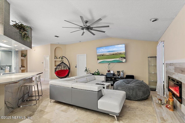 living room featuring a fireplace, a textured ceiling, a ceiling fan, and vaulted ceiling