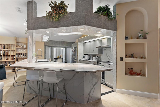 kitchen featuring visible vents, built in shelves, wall chimney range hood, a kitchen breakfast bar, and stainless steel appliances