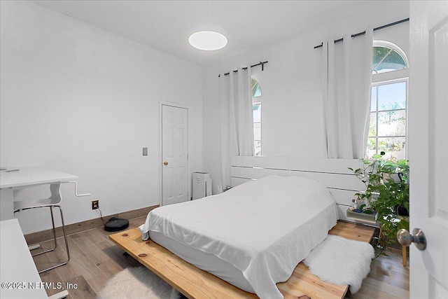 bedroom with radiator heating unit, baseboards, and wood finished floors