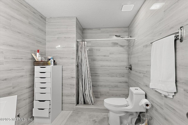 bathroom with a stall shower, toilet, tile walls, and a textured ceiling