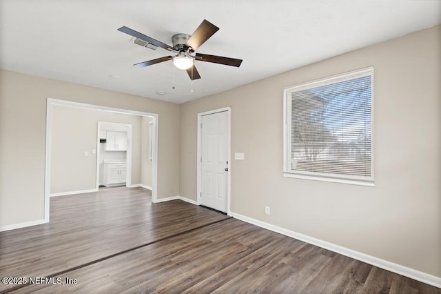 spare room with a ceiling fan, visible vents, baseboards, and wood finished floors