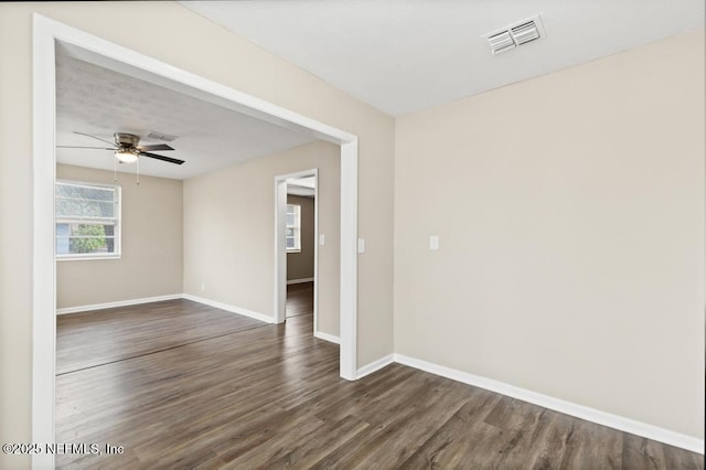 unfurnished room featuring a ceiling fan, visible vents, dark wood finished floors, and baseboards