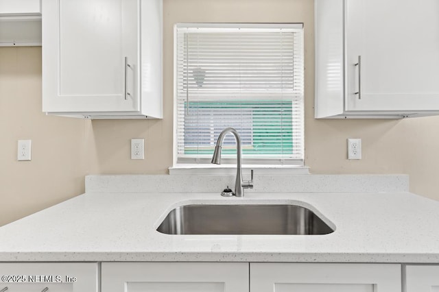 kitchen featuring a sink, light stone countertops, and white cabinets