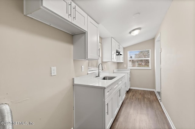 kitchen featuring white cabinets, lofted ceiling, wood finished floors, light countertops, and a sink