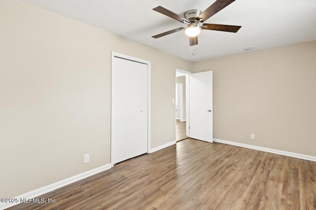 unfurnished bedroom featuring a closet, visible vents, ceiling fan, wood finished floors, and baseboards