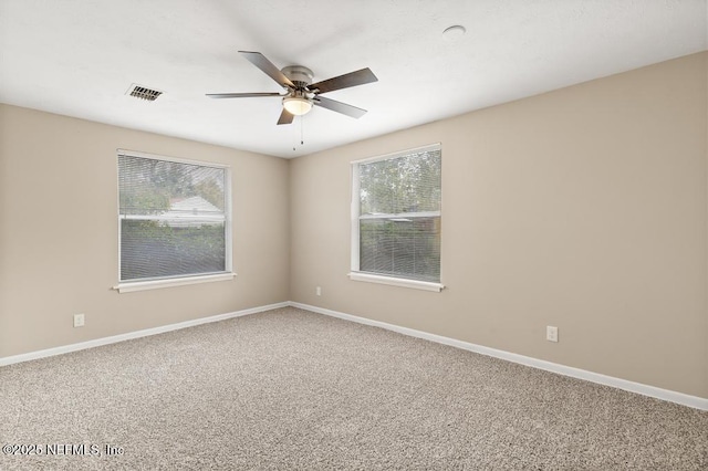 carpeted empty room featuring a wealth of natural light, visible vents, and baseboards