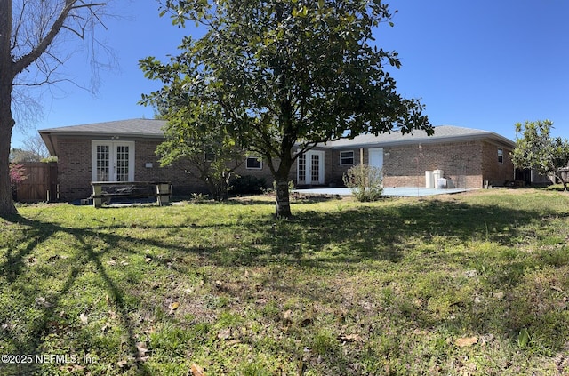 view of front facade with a patio area, french doors, brick siding, and a front yard